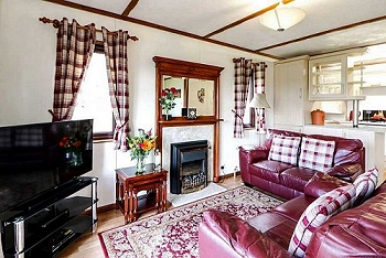 A view showing the living area inside a chalet with two two seater sofas, a fireplace and TV