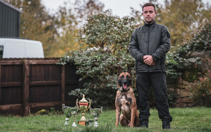 Dog handler with his dog and three trophies