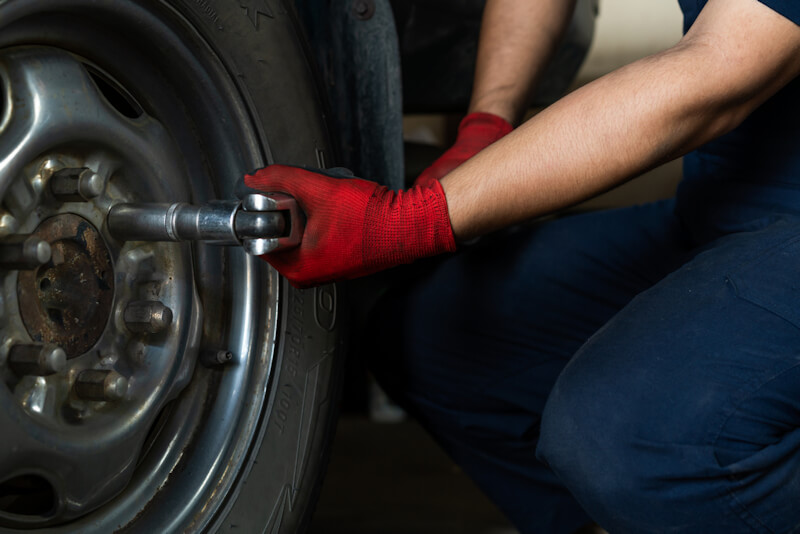 Automotive engineer operating hand tools on car in repair centre, while replacing wheel and tires