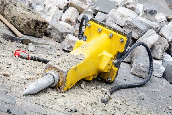 Yellow Hydraulic concrete breaker laying on the ground