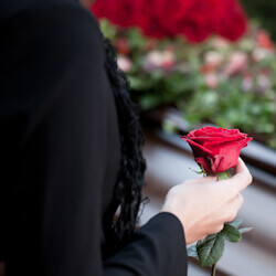 Woman holding red rose in front of coffin at a funeral