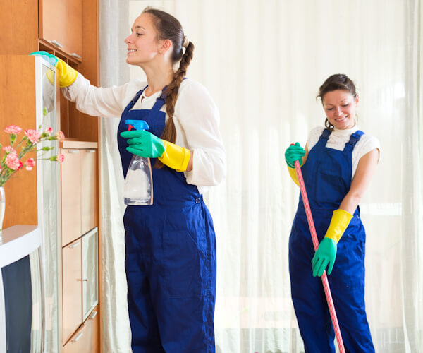 Two female cleaners cleaning kitchen area of a house
