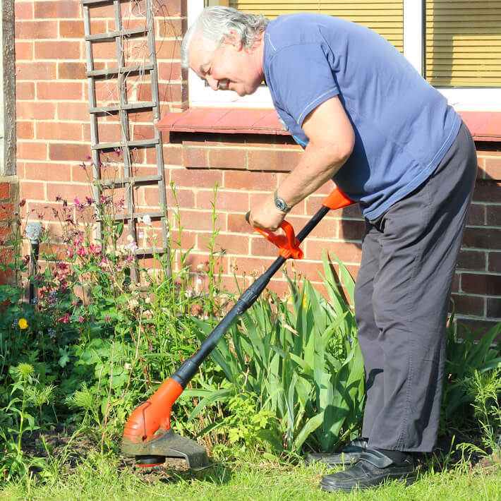 A happy elderly man in his garden with a strimmer cutting his lawn edges