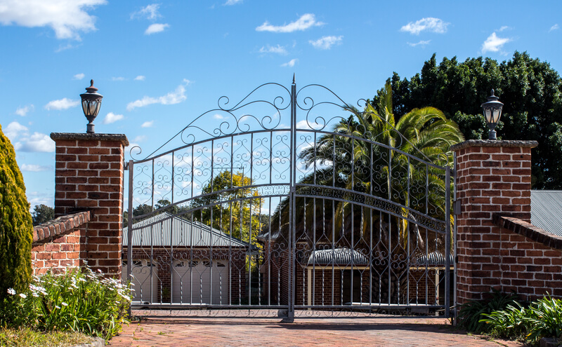 Metal driveway security entrance gates set in brick fence with residential garden