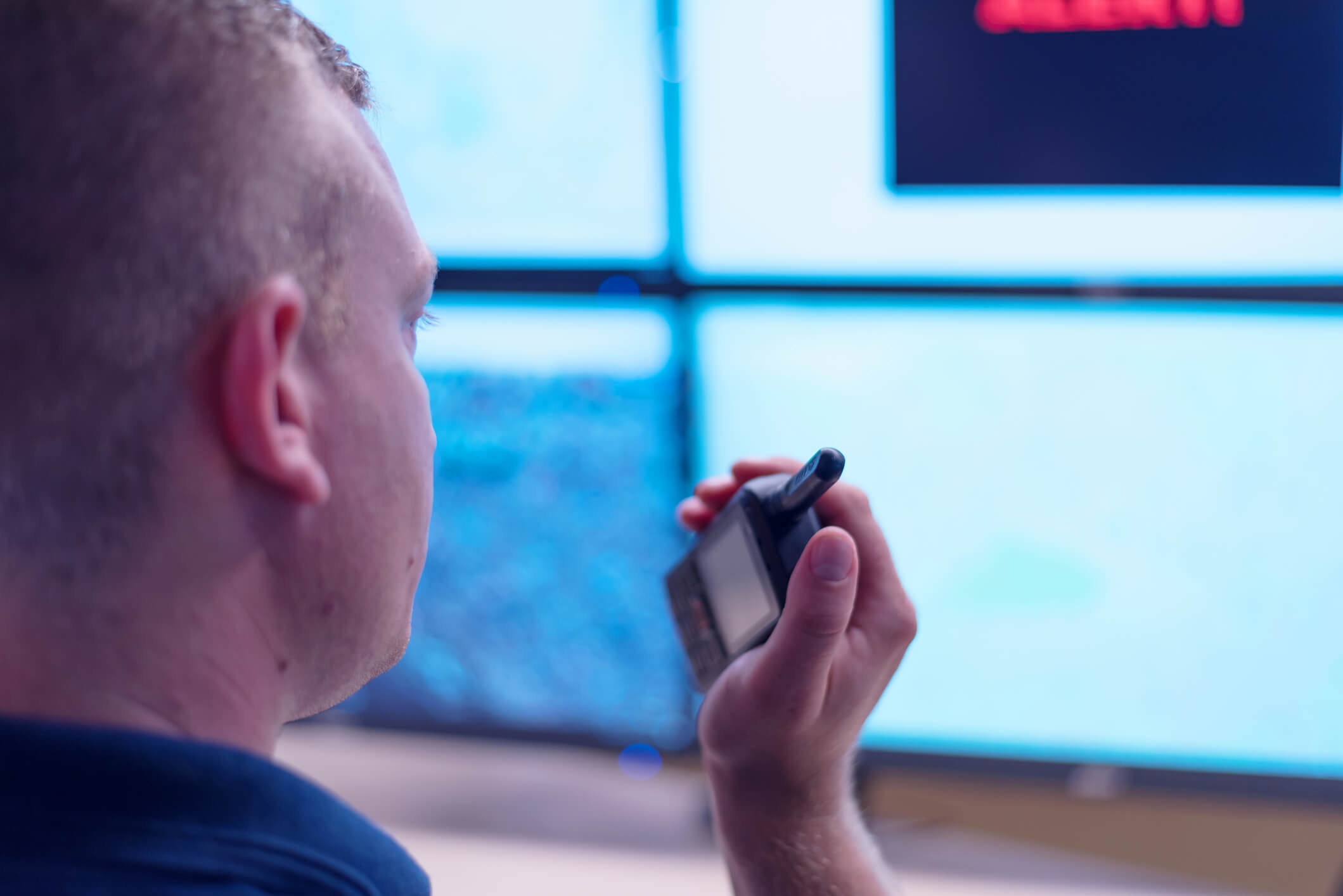 security guard talking over a walkie talkie whilst looking at a bank of surveillance screens