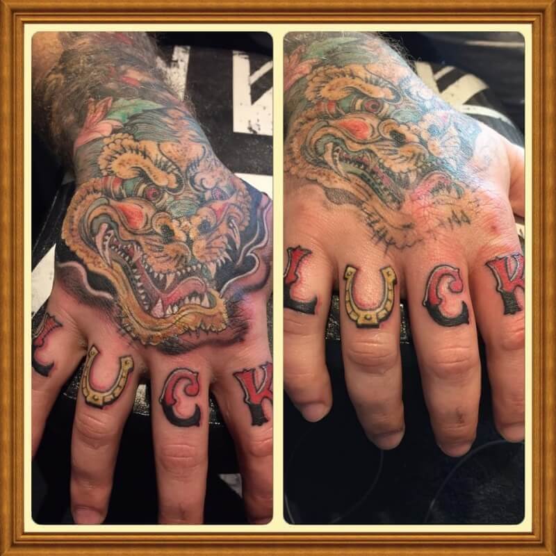 Hand with Japanese dragon and the word luck tattooed.