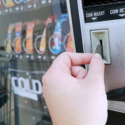 Person inserting coin into vending machine for cold drink
