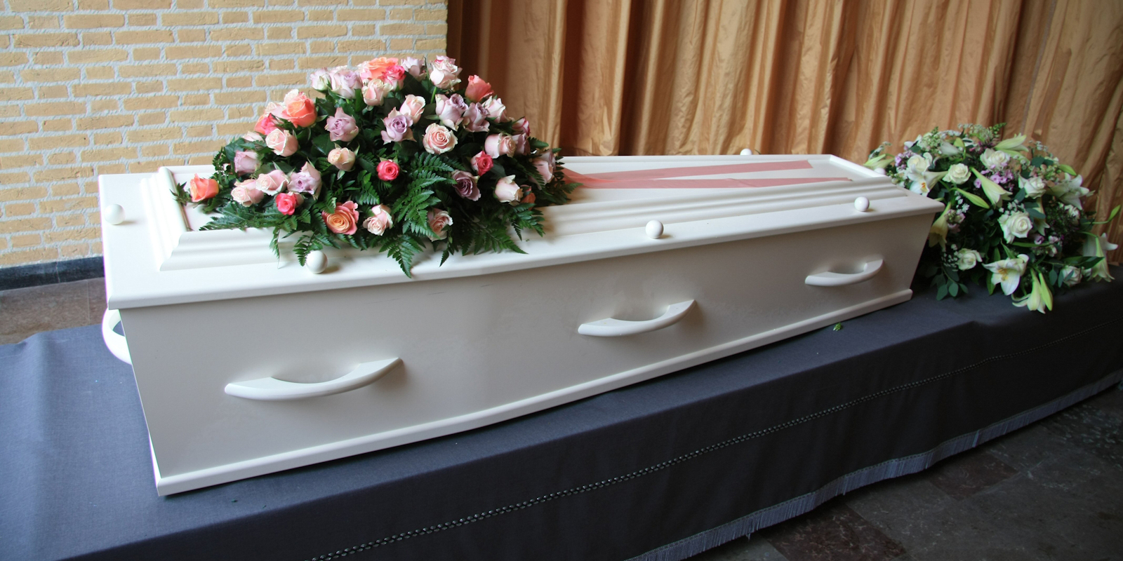 A white coffin with pink flowers at a funeral service