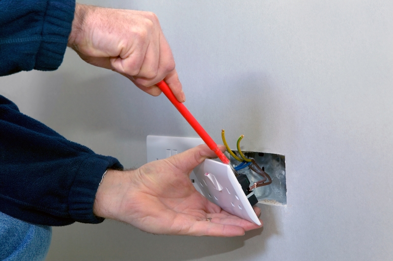 An Electrician Adjusting Wires Behind a Plug Socket