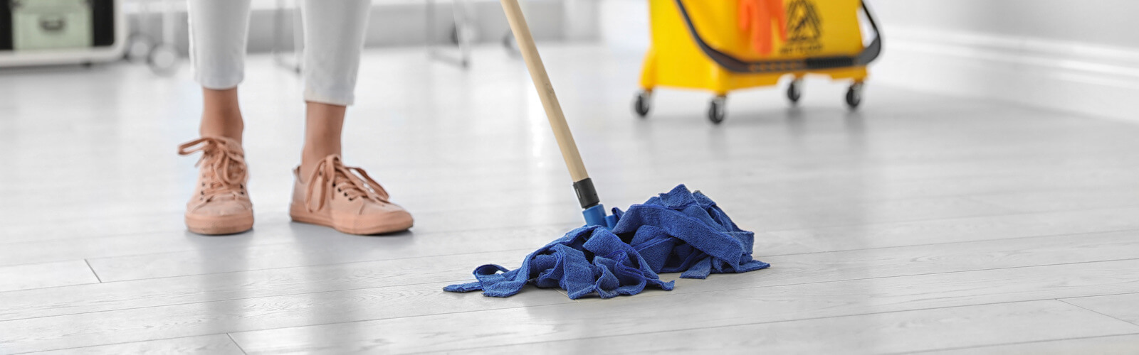 Young woman with mop cleaning floor in office