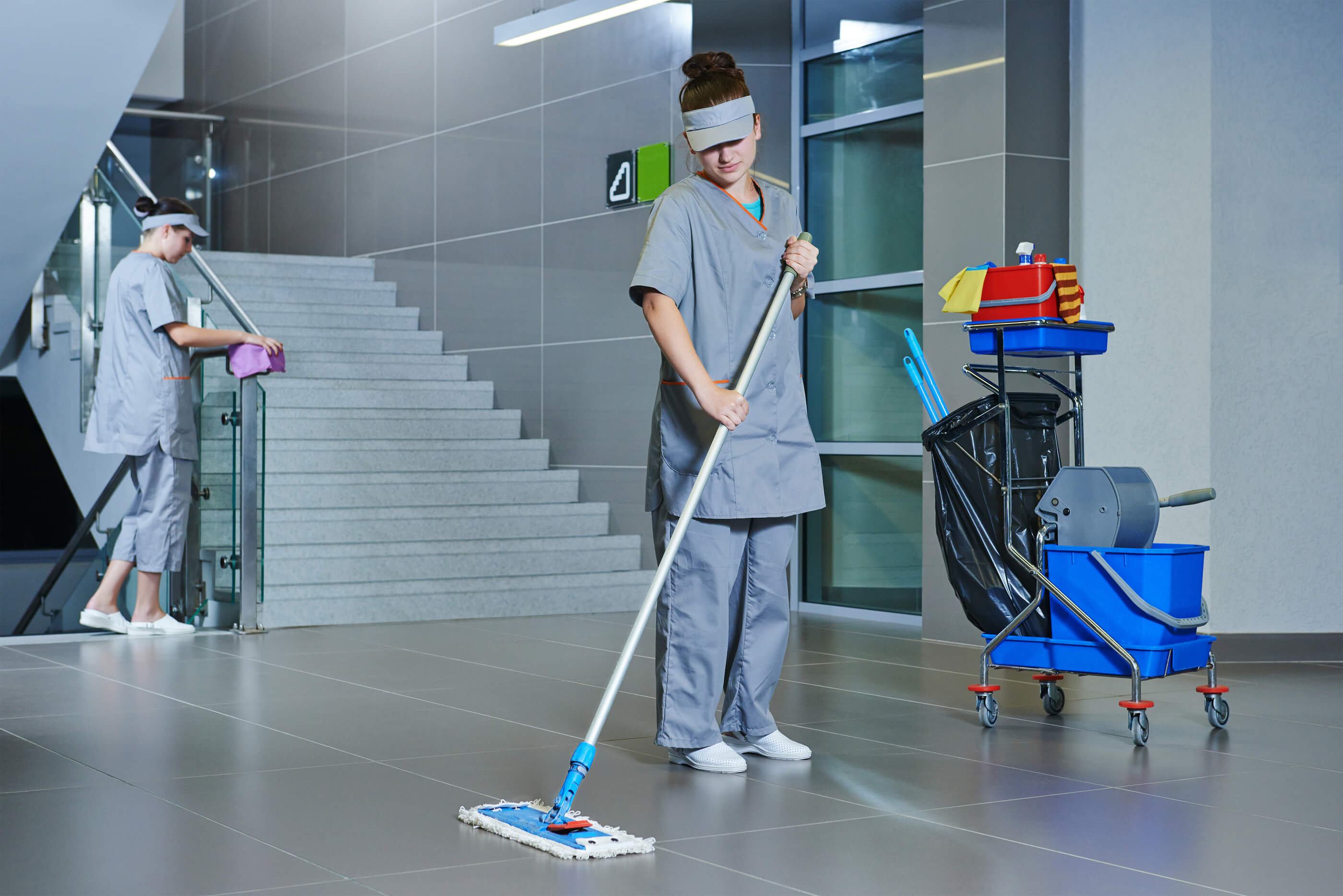 two cleaners, one of which is mopping a hard surface floor and the other is wiping the rails