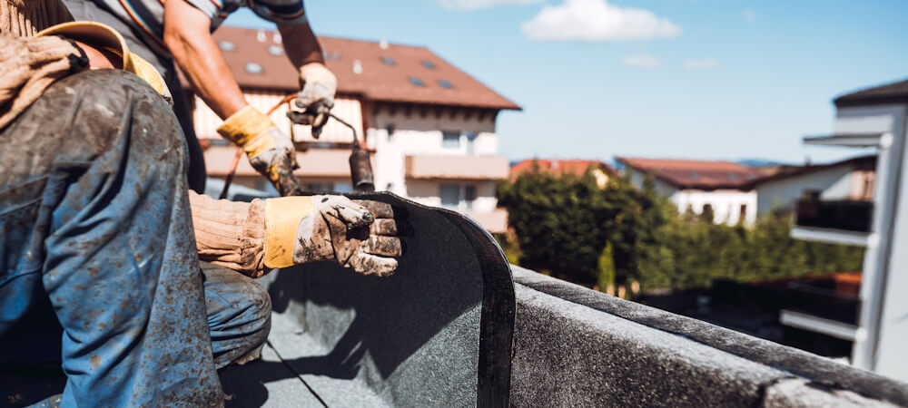 Professional construction worker installing and waterproofing flat roof at construction site